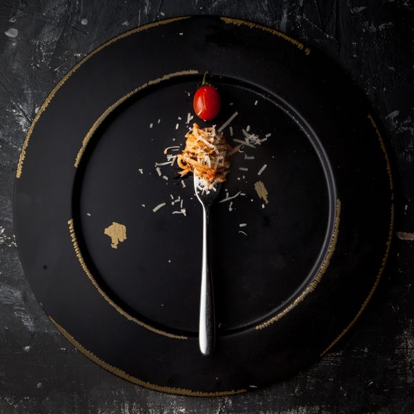 Top view spaghetti with fork and tomato and ricotta cheese in round black plate on stone background